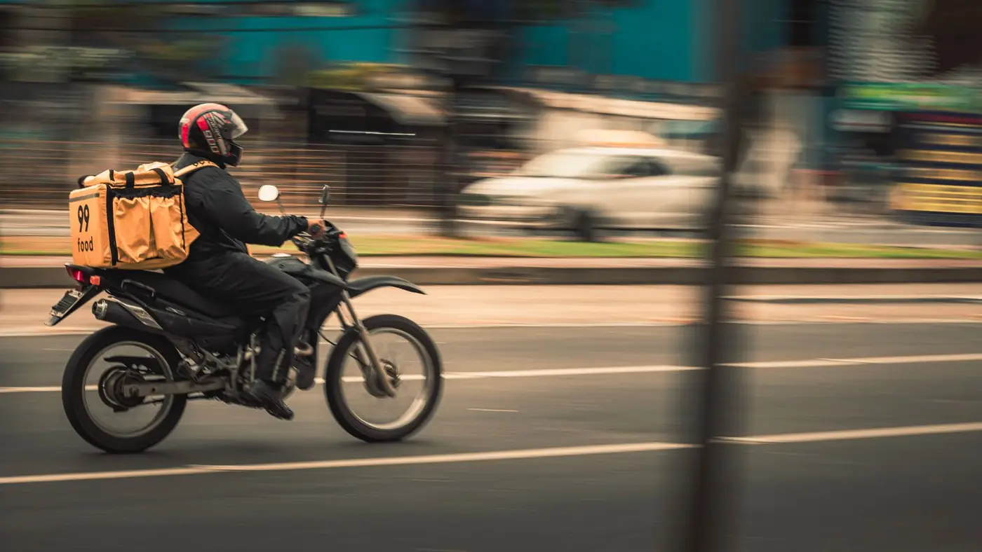 Motoboy de entrega acelerando por uma avenida da cidade